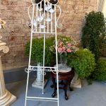 Antique style white wrought iron easel stand with sculpted metal songbird and leafy branches showing adjustable picture display frame in a traditional European parlor interior.