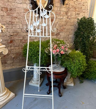 Antique style white wrought iron easel stand with sculpted metal songbird and leafy branches showing adjustable picture display frame in a traditional European parlor interior.