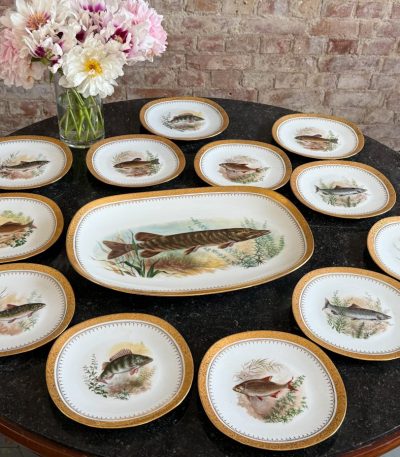 Beautiful limited edition limoges porcelain fish service including a large platter and ten plates with hand-painted fish motifs and heavy gold rims in Naturalism style.