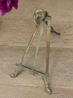 Antique Western style brass tabletop easel featuring a detailed miniature cowboy hat cresting on a folding tripod frame with natural green verdigris patina.