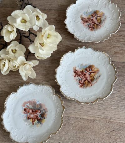 Trīs porcelāna deserta šķīvīši ar putti eņģeļu ainām, reljefu arabesku apmali un