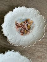 Trīs porcelāna deserta šķīvīši ar putti eņģeļu ainām, reljefu arabesku apmali un zelta malu — Neobaroks / Historicisms, Vācija vai Bohēmija, ap 1880.–1900. gads, 3 gab. (5557) - Image 3