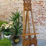 Large vintage studio wood easel with detailed Rococo style hand carvings on the cresting and base plinth.